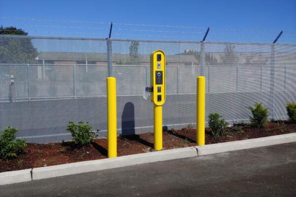 Yellow card reader pedestal between safety bollards along a security fence