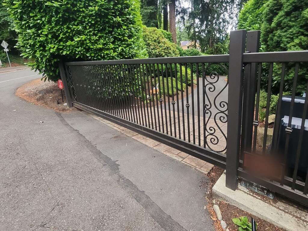 Black ornamental metal slide gate with scroll detail across a residential driveway