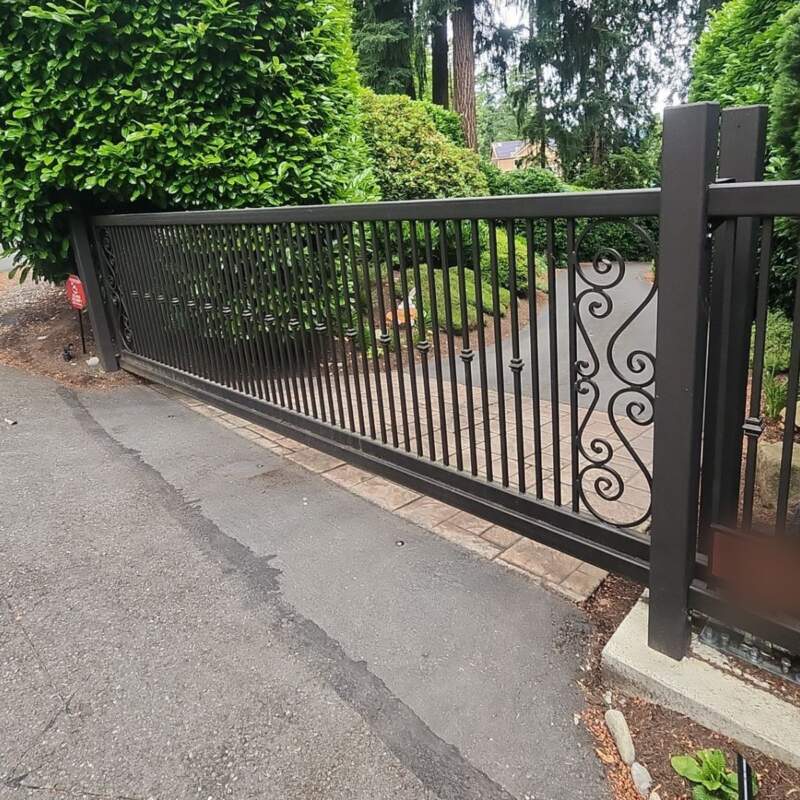Black ornamental metal slide gate with scroll detail across a residential driveway
