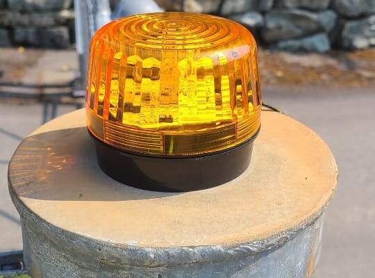 Amber warning strobe light mounted on top of a gate post